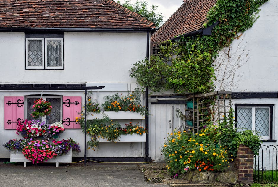 A shaded garden entrance framed by lush green foliage, with a dirt pathway leading through dense trees and shrubs. The sunlight filters through the leaves, casting dappled shadows on the ground. To th